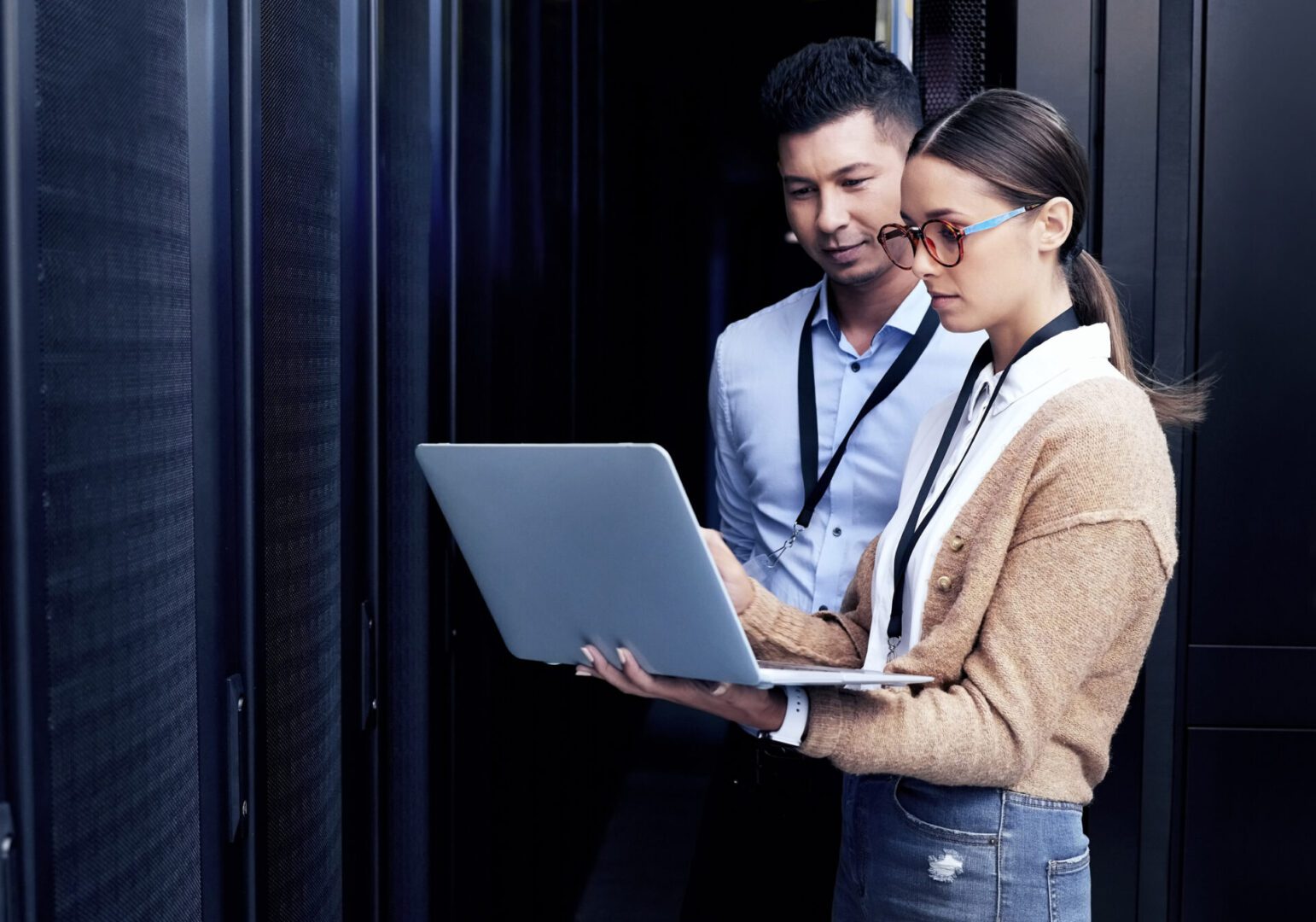 Two professionals reviewing data on a laptop in a server room.