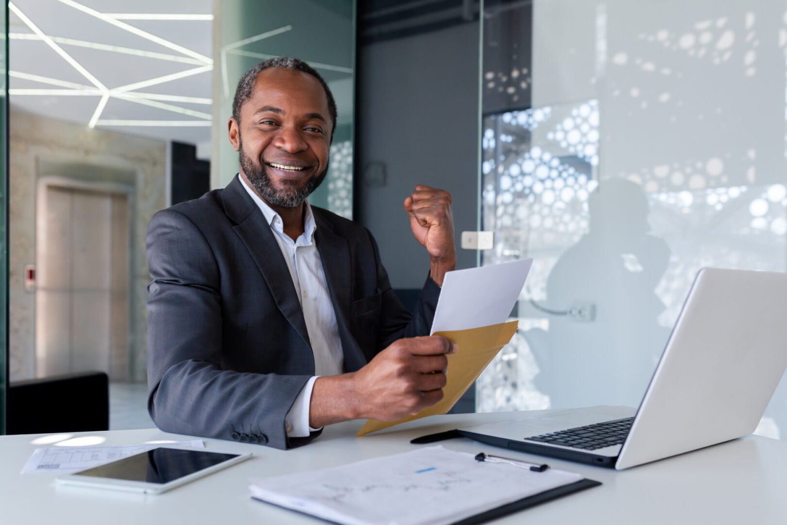 Smiling businessman holding documents at desk in modern office.