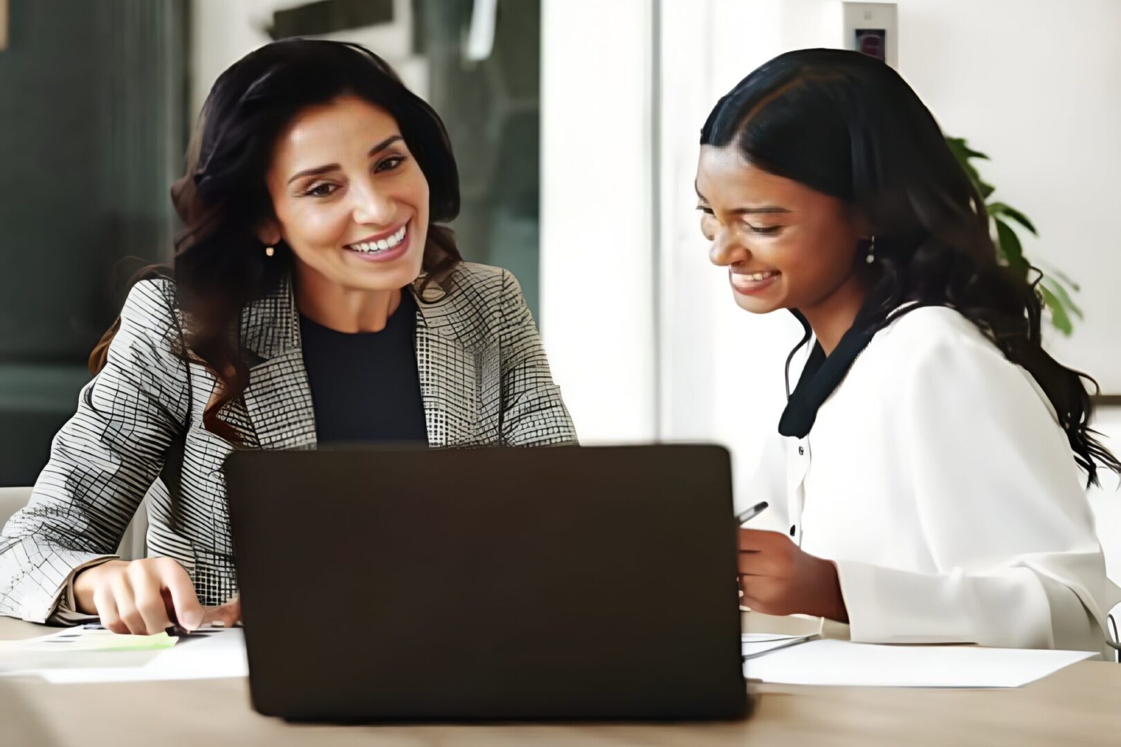 Two women collaborating on a laptop, smiling and engaged.