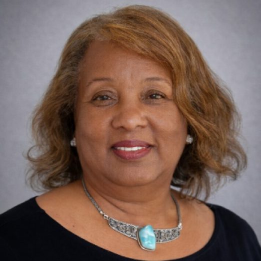 Portrait of a smiling woman with light brown hair and a turquoise necklace.