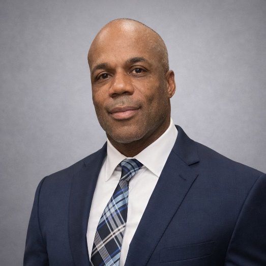 Professional portrait of a man in a suit and tie against a gray backdrop.